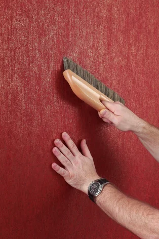 Illustration - Ihr Experte für schönes Wohnen - Ein Handwerker streicht mit einer Tapetenbürste die Tapete glatt, so dass keine Luftblasen mehr unter der Tapete sind.