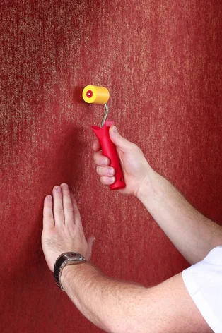 Illustration - Ihr Experte für schönes Wohnen - Ein Handwerker rollt mit einer speziellen Rolle über die Naht der Tapeten, damit diese gut verschlossen und nicht mehr sichtbar ist.
